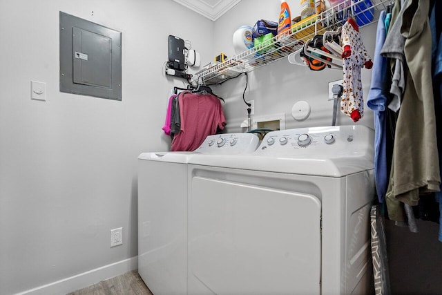 clothes washing area featuring electric panel, light hardwood / wood-style floors, washing machine and dryer, and ornamental molding