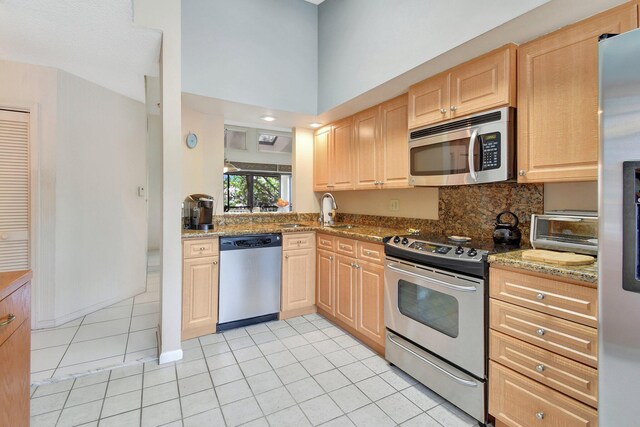 kitchen featuring light brown cabinets, light stone countertops, light tile patterned floors, and appliances with stainless steel finishes