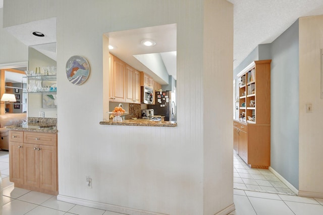 kitchen featuring light stone counters, stainless steel appliances, a textured ceiling, light tile patterned floors, and light brown cabinets