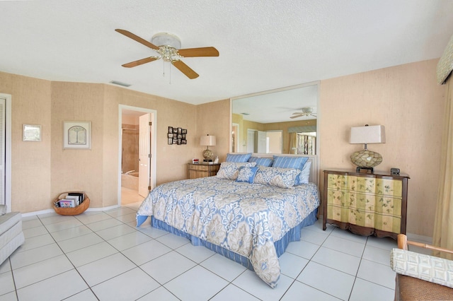 bedroom with ceiling fan, connected bathroom, light tile patterned floors, and a textured ceiling