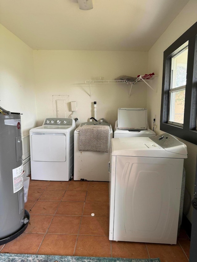 laundry area with electric water heater, washing machine and clothes dryer, and dark tile patterned flooring