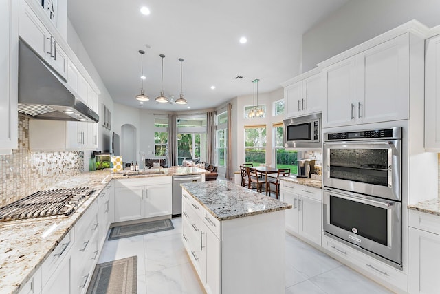 kitchen featuring tasteful backsplash, light stone counters, stainless steel appliances, white cabinets, and hanging light fixtures