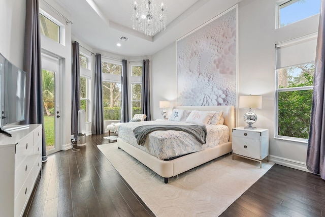 bedroom featuring dark wood-type flooring, a high ceiling, an inviting chandelier, a raised ceiling, and access to outside