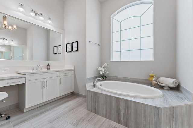 bathroom featuring vanity, tiled tub, and a chandelier