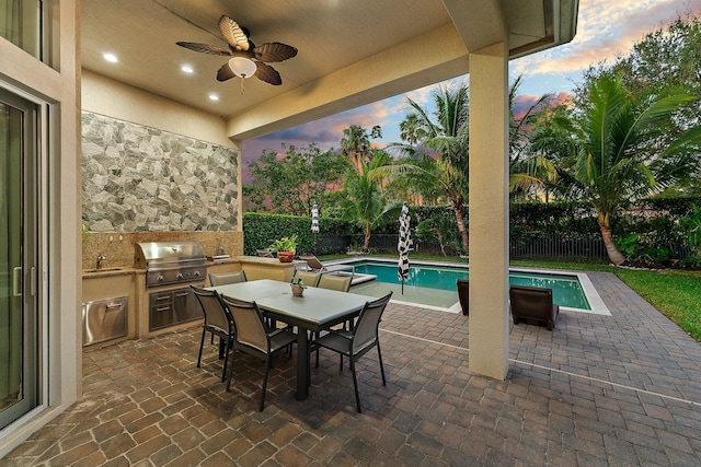 patio terrace at dusk featuring ceiling fan, sink, grilling area, a fenced in pool, and area for grilling