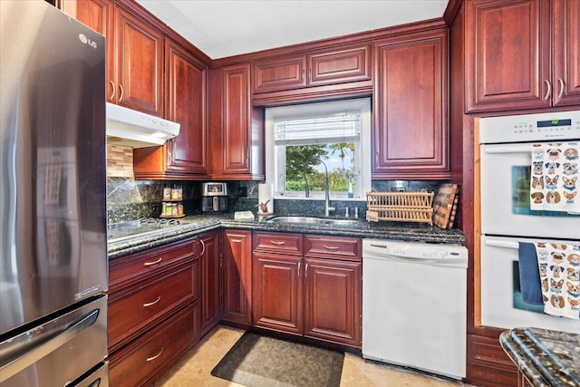 kitchen featuring white appliances, backsplash, dark stone counters, and sink