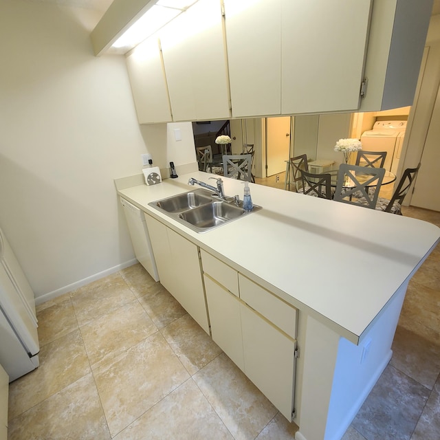 kitchen with cream cabinets, white dishwasher, kitchen peninsula, sink, and washer / dryer