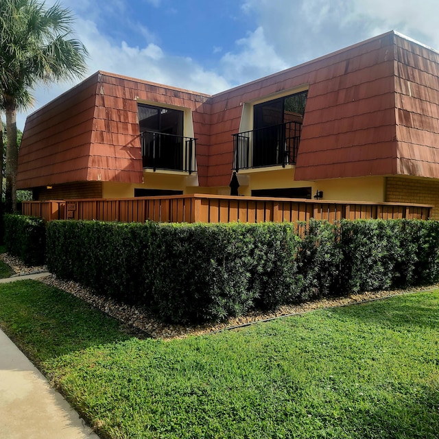 view of side of home with mansard roof, a yard, brick siding, and a balcony