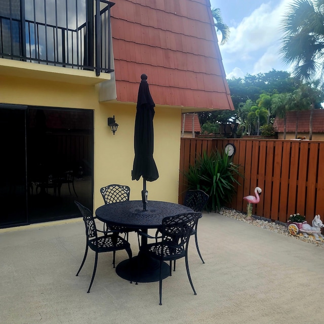 view of patio featuring outdoor dining space, a balcony, and fence