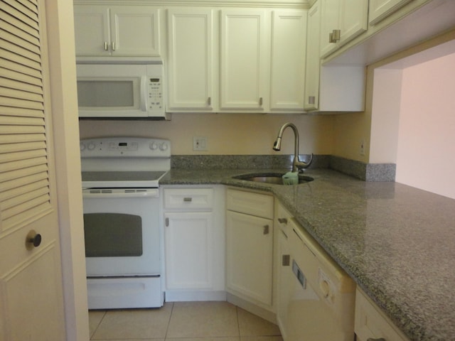 kitchen with light tile patterned floors, white appliances, dark stone countertops, and sink