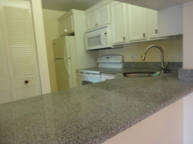 kitchen with a textured ceiling, white appliances, sink, white cabinets, and kitchen peninsula