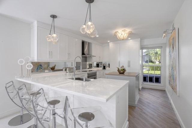 kitchen with wall chimney range hood, kitchen peninsula, white cabinets, and a kitchen bar