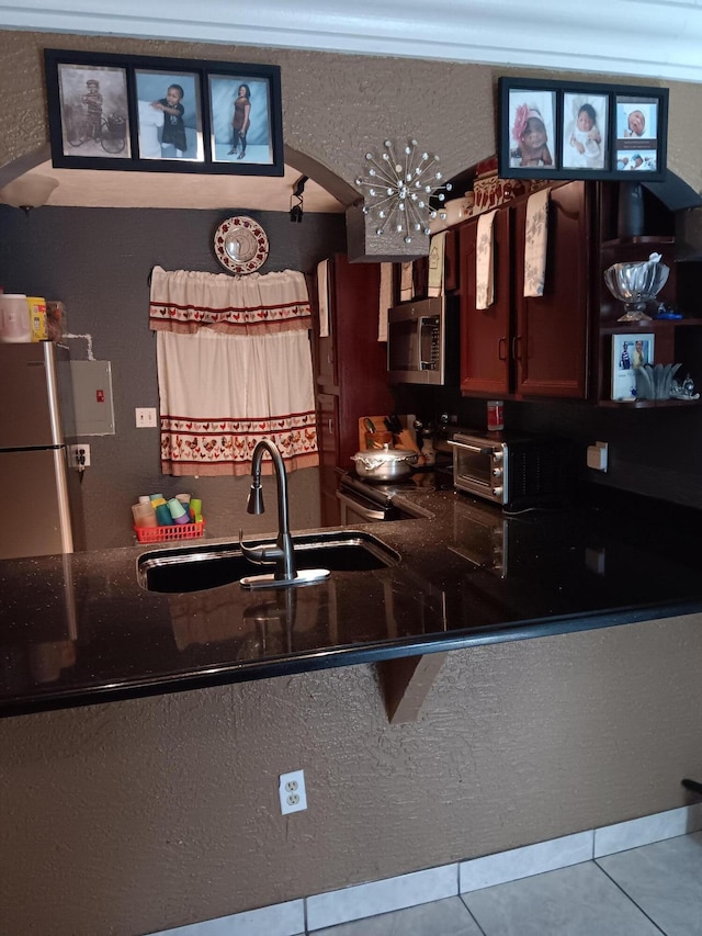 kitchen featuring tile patterned flooring, dark stone countertops, sink, and appliances with stainless steel finishes