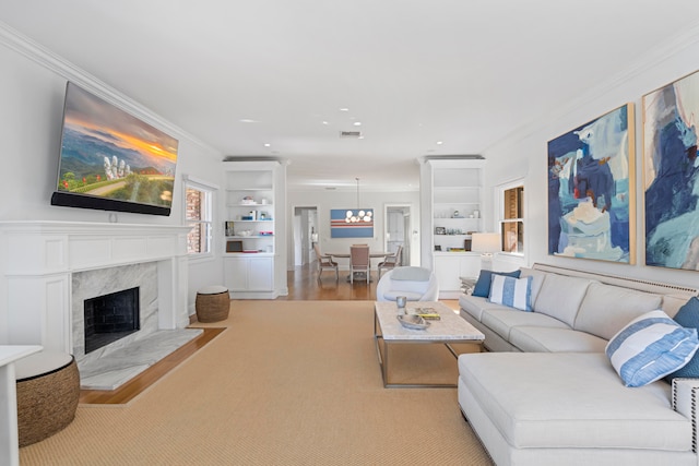 living room featuring crown molding, built in features, a premium fireplace, a chandelier, and light hardwood / wood-style floors