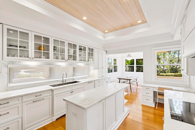 kitchen featuring light stone countertops, sink, a tray ceiling, white cabinets, and light wood-type flooring