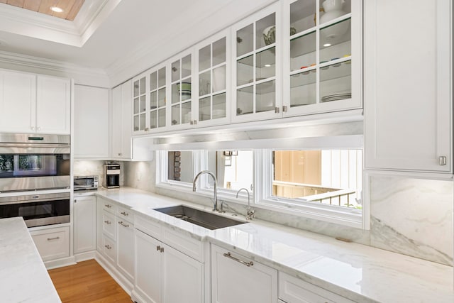 kitchen featuring white cabinets, light stone counters, stainless steel double oven, and sink