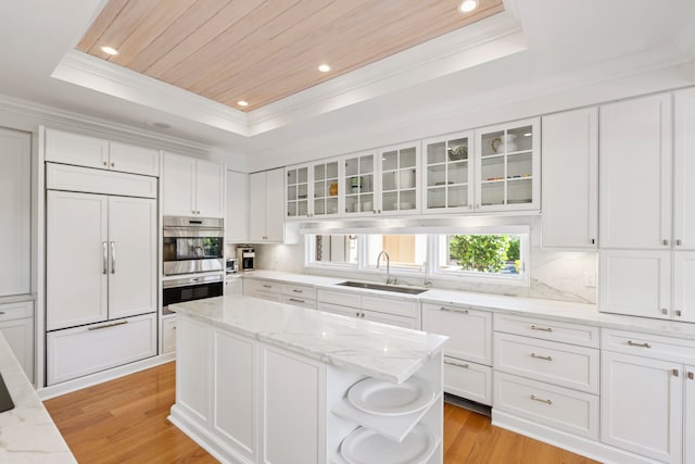 kitchen with light hardwood / wood-style flooring, paneled refrigerator, sink, and a tray ceiling