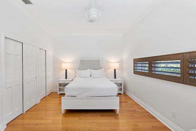 bedroom featuring multiple closets, crown molding, ceiling fan, and light hardwood / wood-style floors