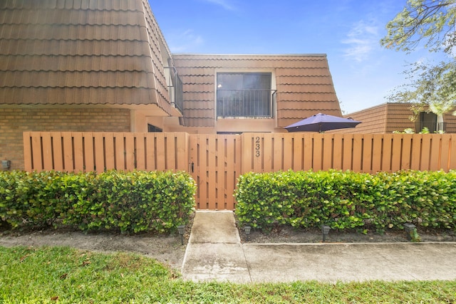 233 Charter Way, West Palm Beach, FL 33407 - view of home's exterior with brick siding, a fenced front yard, a tiled roof, and mansard roof