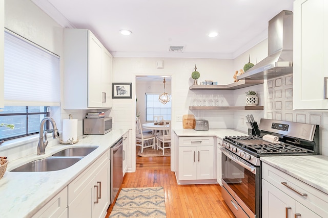 kitchen with stainless steel appliances, white cabinets, sink, wall chimney range hood, and light wood-type flooring