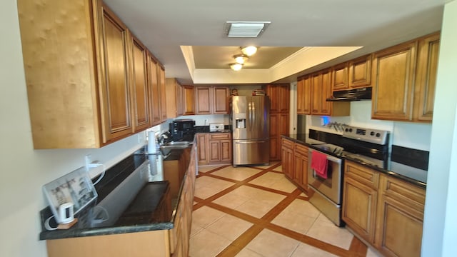 kitchen with sink, dark stone counters, a tray ceiling, light tile patterned floors, and appliances with stainless steel finishes