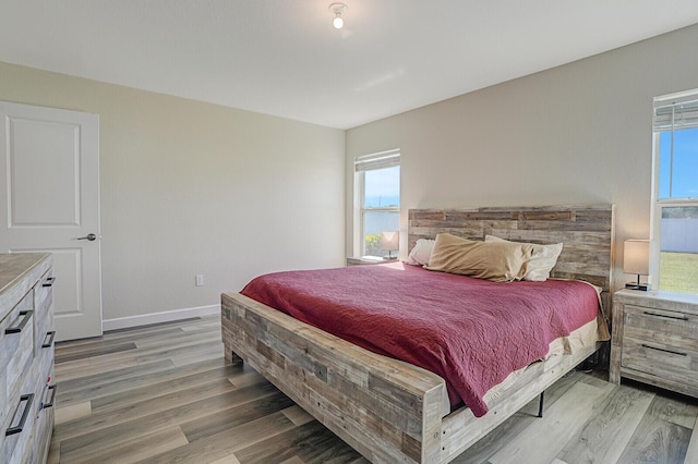 bedroom with multiple windows, wood finished floors, and baseboards