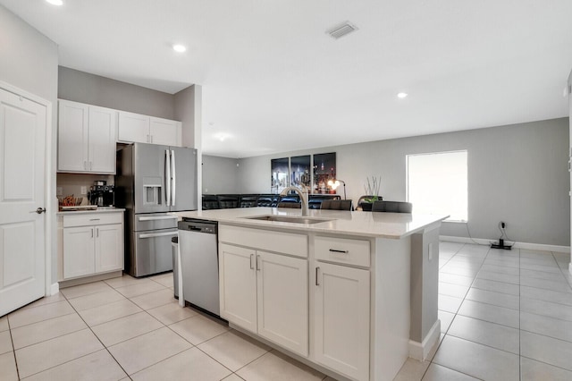 kitchen featuring a kitchen island with sink, stainless steel appliances, a sink, white cabinetry, and light countertops