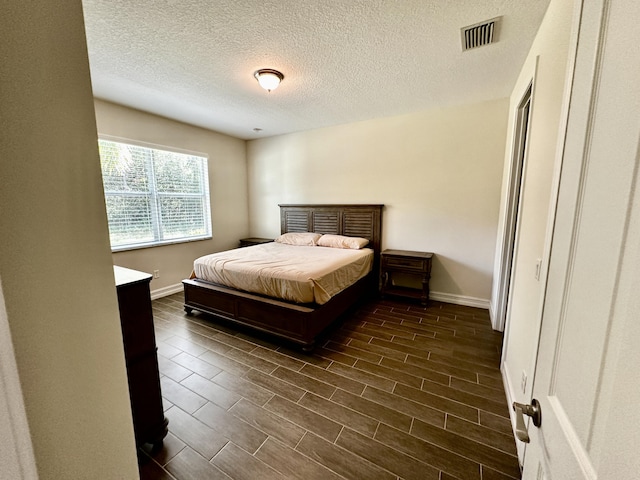 bedroom featuring a textured ceiling, wood finish floors, visible vents, and baseboards