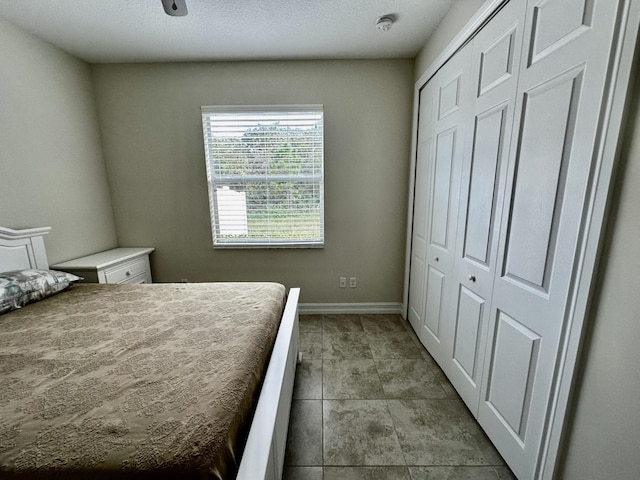 bedroom featuring a closet, a textured ceiling, baseboards, and light tile patterned floors