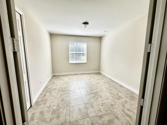 unfurnished room with a textured ceiling, light tile patterned flooring, visible vents, and baseboards