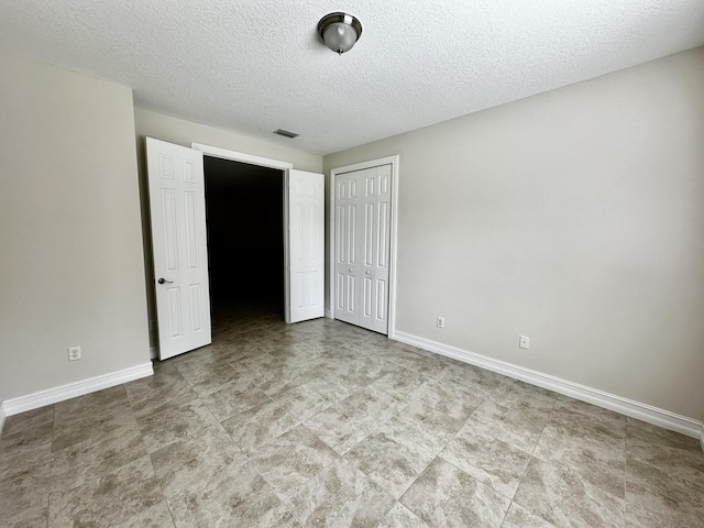 unfurnished bedroom featuring a closet, visible vents, a textured ceiling, and baseboards