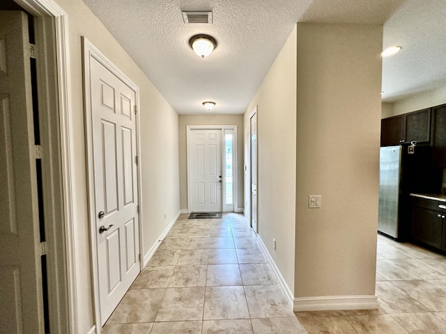 entryway with visible vents, a textured ceiling, baseboards, and light tile patterned floors