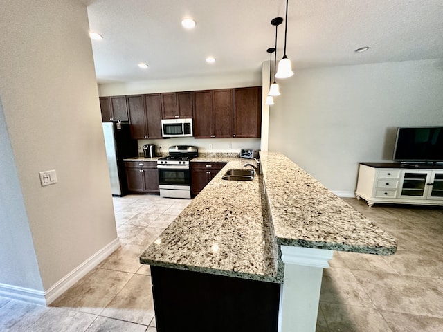 kitchen featuring a peninsula, a sink, stainless steel gas range, freestanding refrigerator, and decorative light fixtures