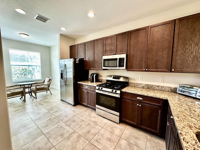 kitchen with visible vents, appliances with stainless steel finishes, light stone counters, and dark brown cabinetry