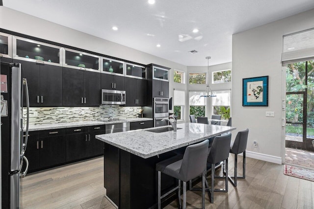 kitchen with stainless steel appliances, pendant lighting, sink, an island with sink, and light hardwood / wood-style floors