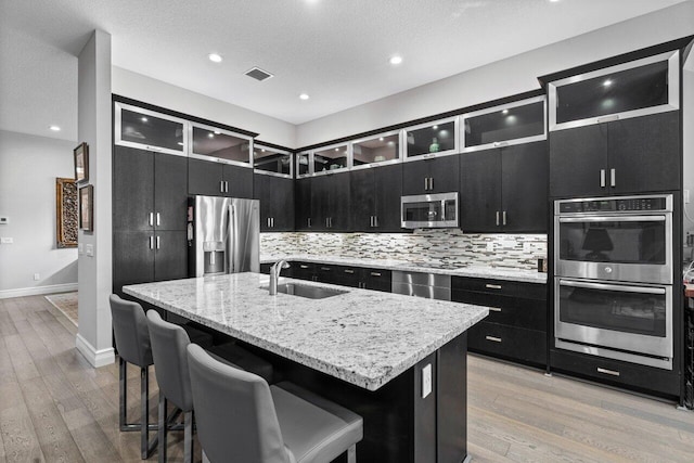 kitchen featuring sink, appliances with stainless steel finishes, a kitchen bar, an island with sink, and light wood-type flooring