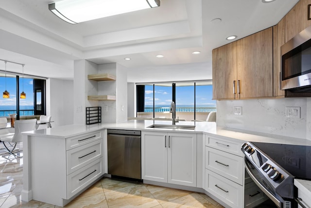 kitchen featuring white cabinetry, sink, kitchen peninsula, a water view, and appliances with stainless steel finishes