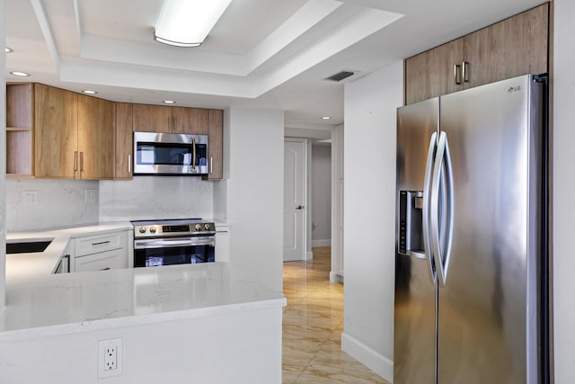 kitchen featuring kitchen peninsula, appliances with stainless steel finishes, a tray ceiling, and light stone counters