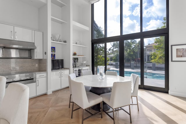 dining space with built in shelves, a towering ceiling, a wealth of natural light, and light parquet floors