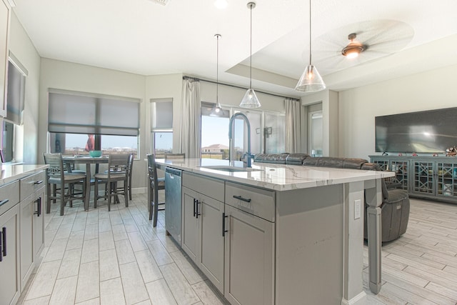 kitchen with light stone counters, hanging light fixtures, a kitchen breakfast bar, and an island with sink