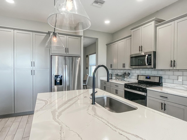 kitchen with appliances with stainless steel finishes, decorative light fixtures, sink, gray cabinetry, and light stone counters