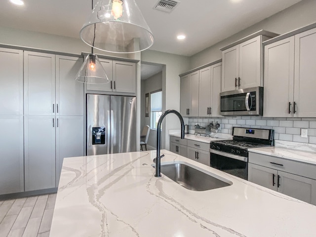 kitchen featuring sink, tasteful backsplash, gray cabinets, pendant lighting, and stainless steel appliances