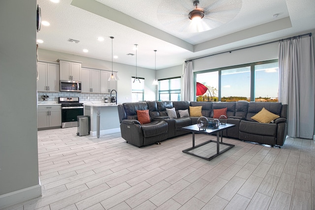 living room with sink, a textured ceiling, light hardwood / wood-style flooring, a raised ceiling, and ceiling fan