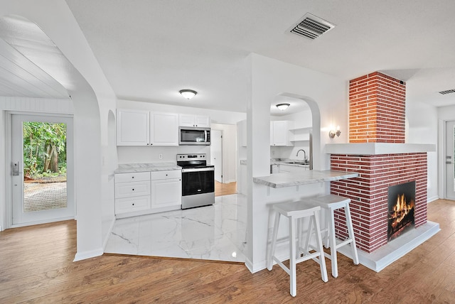 kitchen with stainless steel appliances, kitchen peninsula, a breakfast bar, white cabinets, and light wood-type flooring