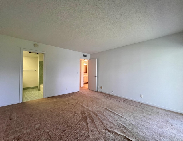 unfurnished bedroom featuring ensuite bathroom, a textured ceiling, and light carpet