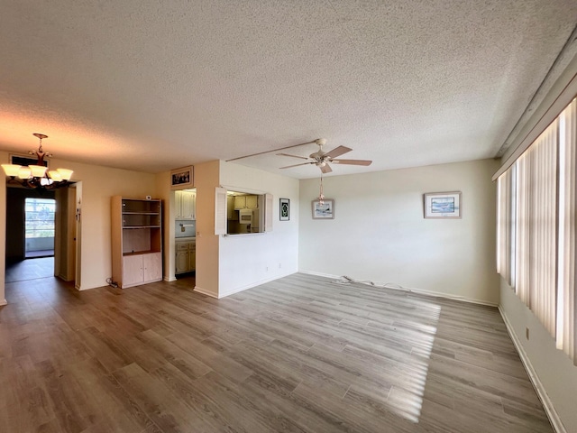 unfurnished living room with hardwood / wood-style floors, ceiling fan with notable chandelier, and a textured ceiling