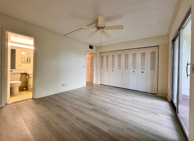 unfurnished bedroom with light wood-type flooring, a textured ceiling, ceiling fan, and ensuite bath