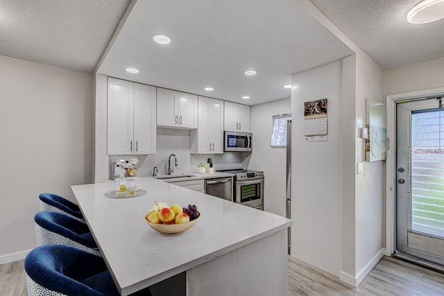 kitchen with kitchen peninsula, appliances with stainless steel finishes, sink, white cabinets, and light hardwood / wood-style floors