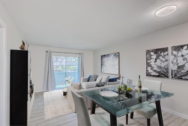 dining room featuring a textured ceiling, baseboards, and light wood-type flooring