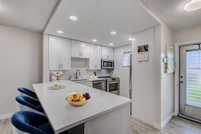 kitchen featuring light countertops, a sink, light wood-style flooring, stainless steel appliances, and white cabinets